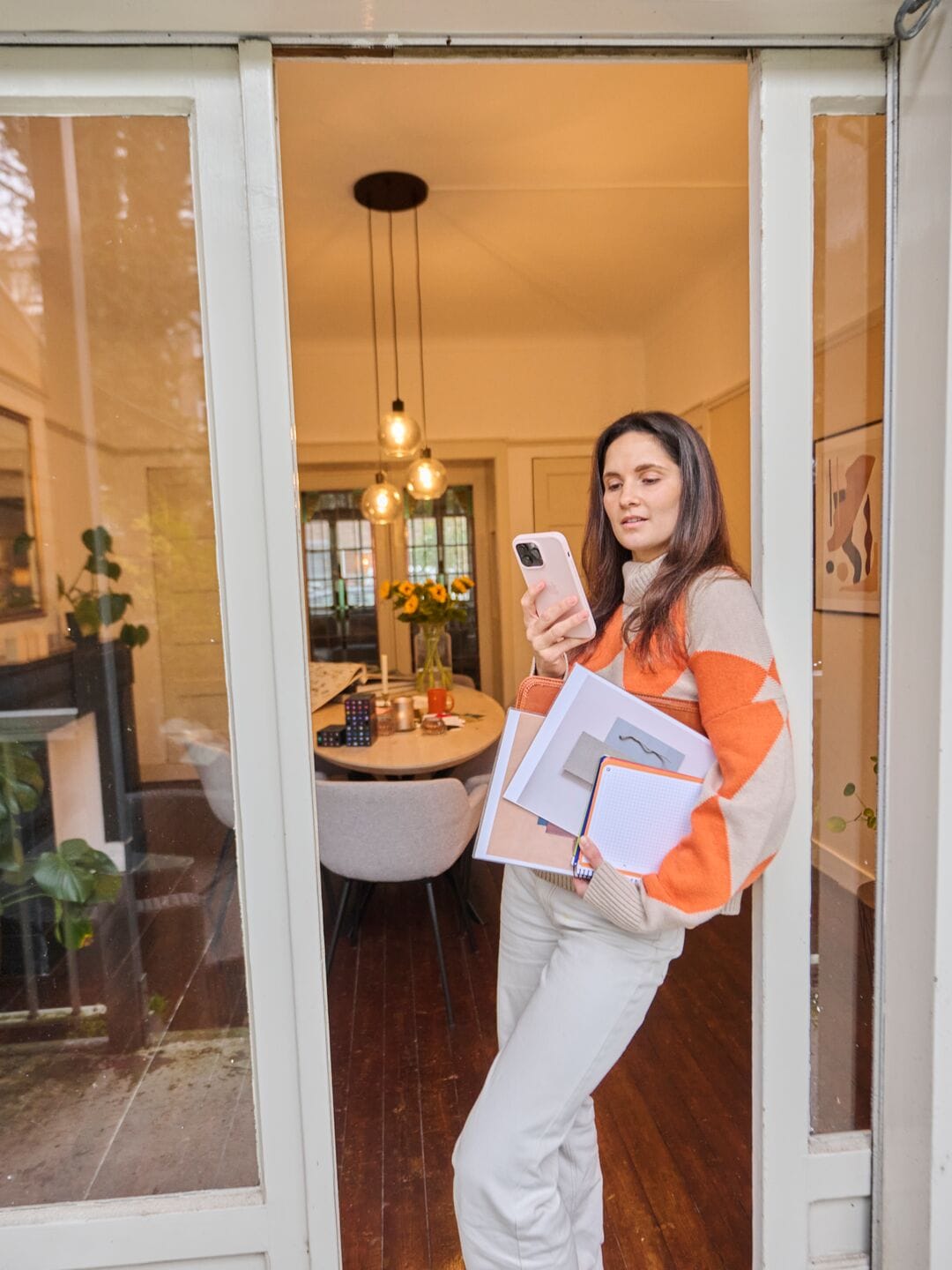 Interior designer working from home with papers, a laptop and her phone, stands by the window