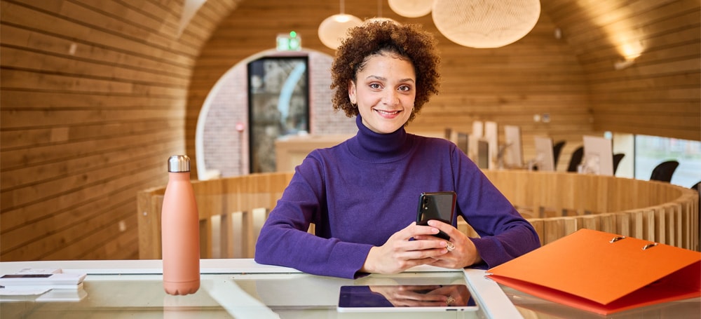 Vrouw zit aan een tafel en werkt op haar laptop in een openbare werkplek op kantoor