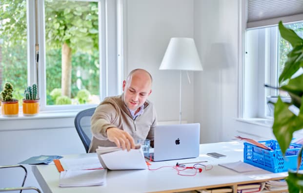 man met documenten achter zijn laptop