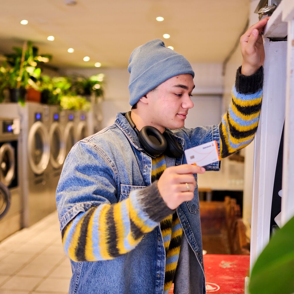 Young man/student in a laundromat holding a bank card in his hand.
