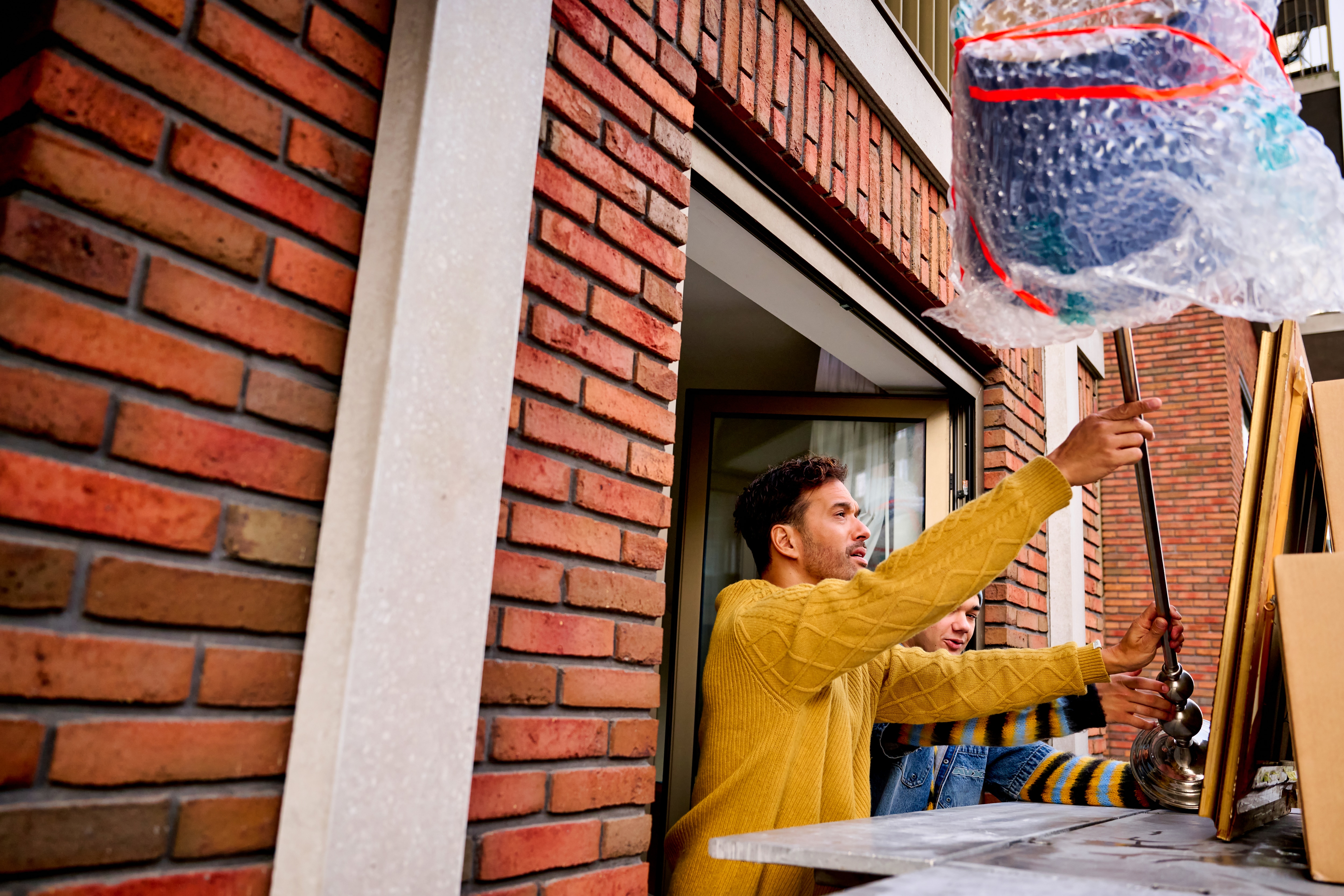 Man in a yellow sweater placing moving boxes onto a moving lift through a window.