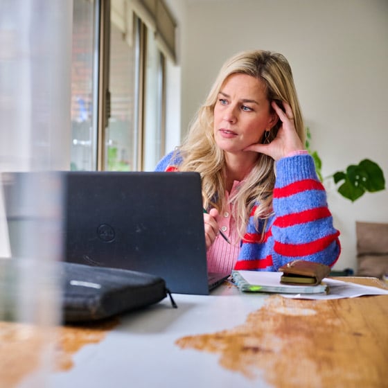 Vrouw zit achter haar laptop en kijkt een beetje dromerig naar buiten