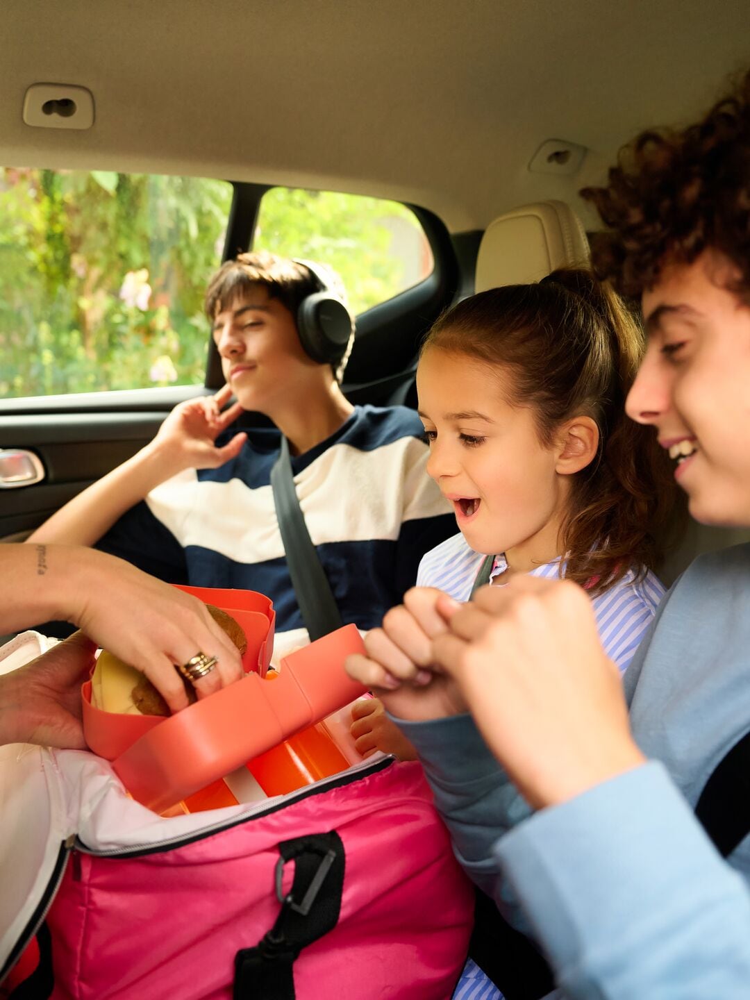Young children in the back seat of the car receiving something to eat, while the mother is turned around handing it out.”