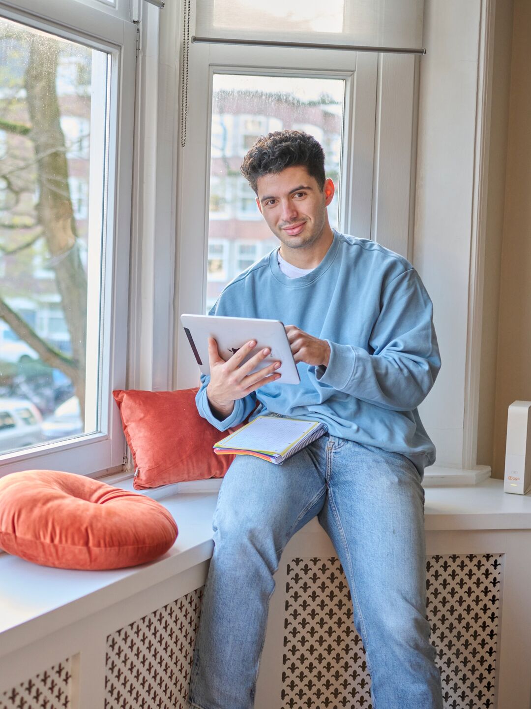 Young man studying while sitting in windowsill at home