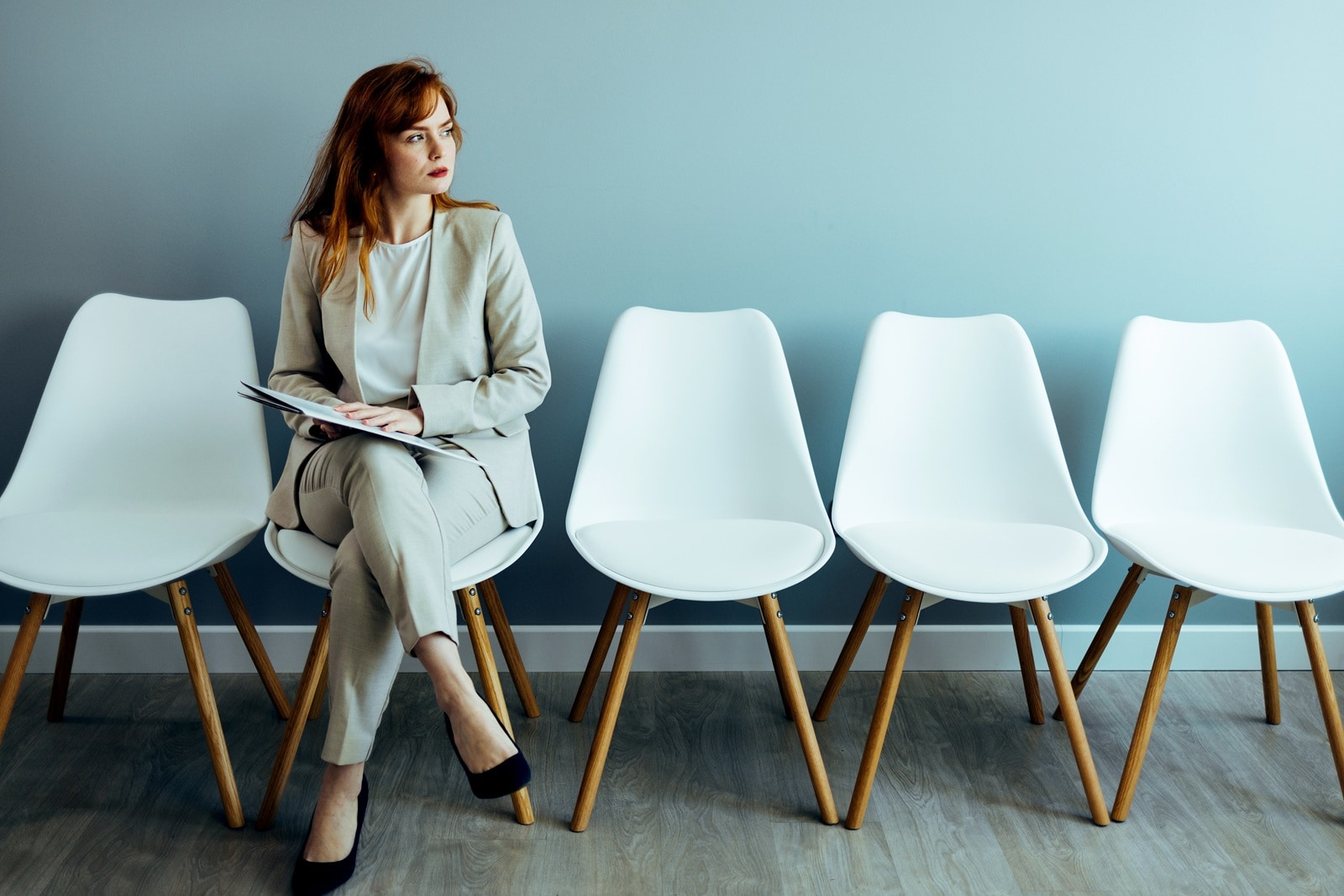 Vijf witte stoelen met op één ervan een vrouw in pak.