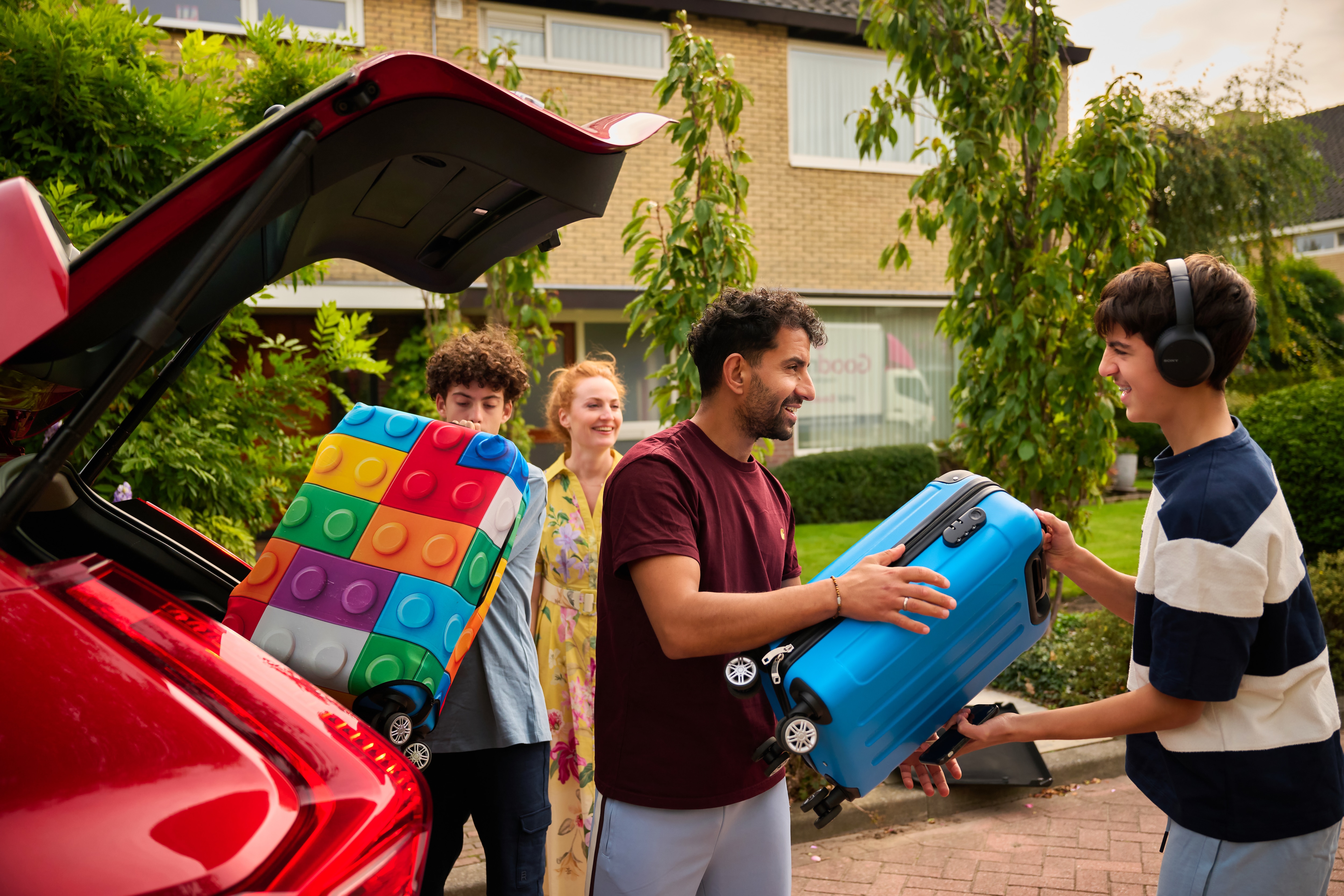 Parents and teens (up to 15) unpacking suitcases from the car after a trip.