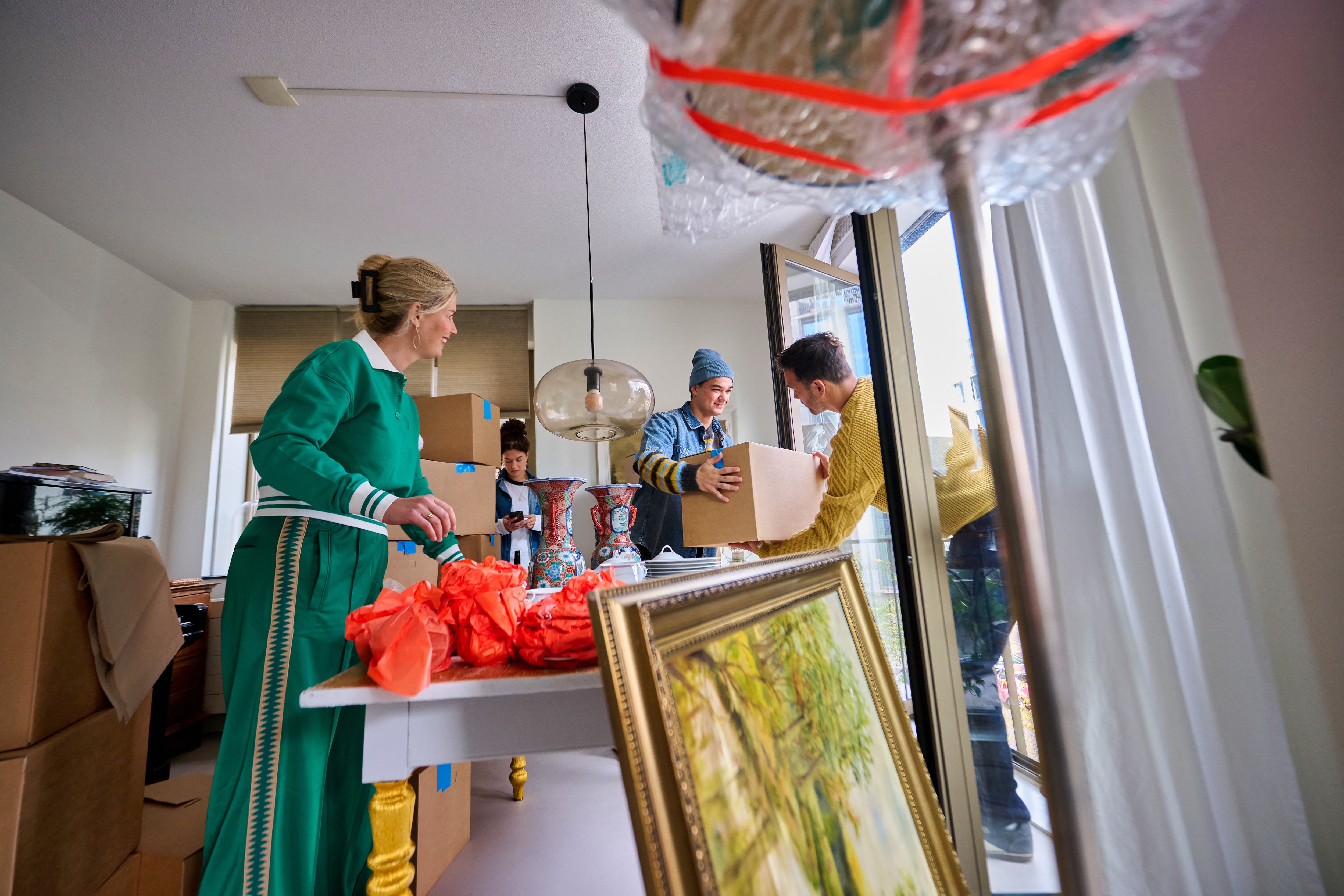 Family standing in a living room, passing moving boxes to each other and unpacking items.