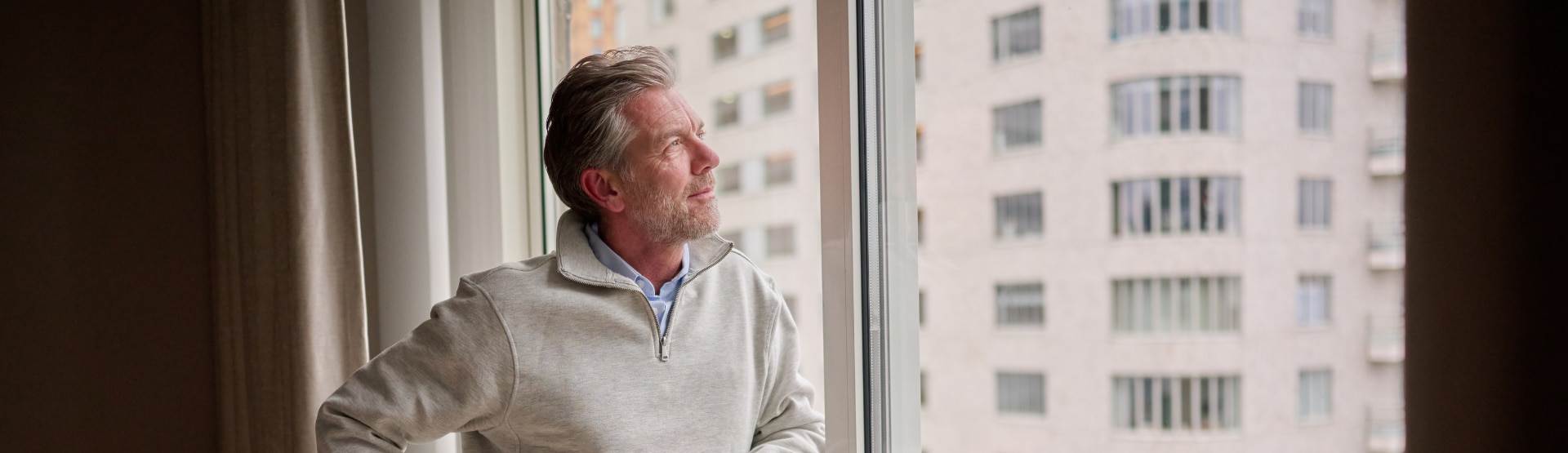 Vermogende man uit een familieonderneming kijkt uit het raam van zijn luxe appartement.