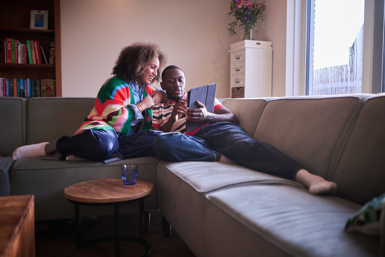 Man en vrouw zitten op de bank in een woonkamer en bekijken samen papieren documenten op tablet