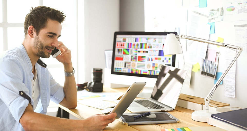 Man telefoneert achter zijn bureau met een tablet in z'n hand