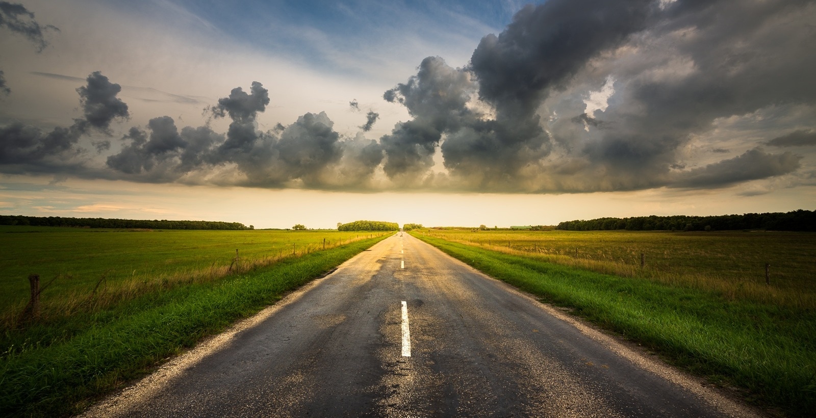 rechte weg bij zonsondergang met donkere wolken aan de horizon