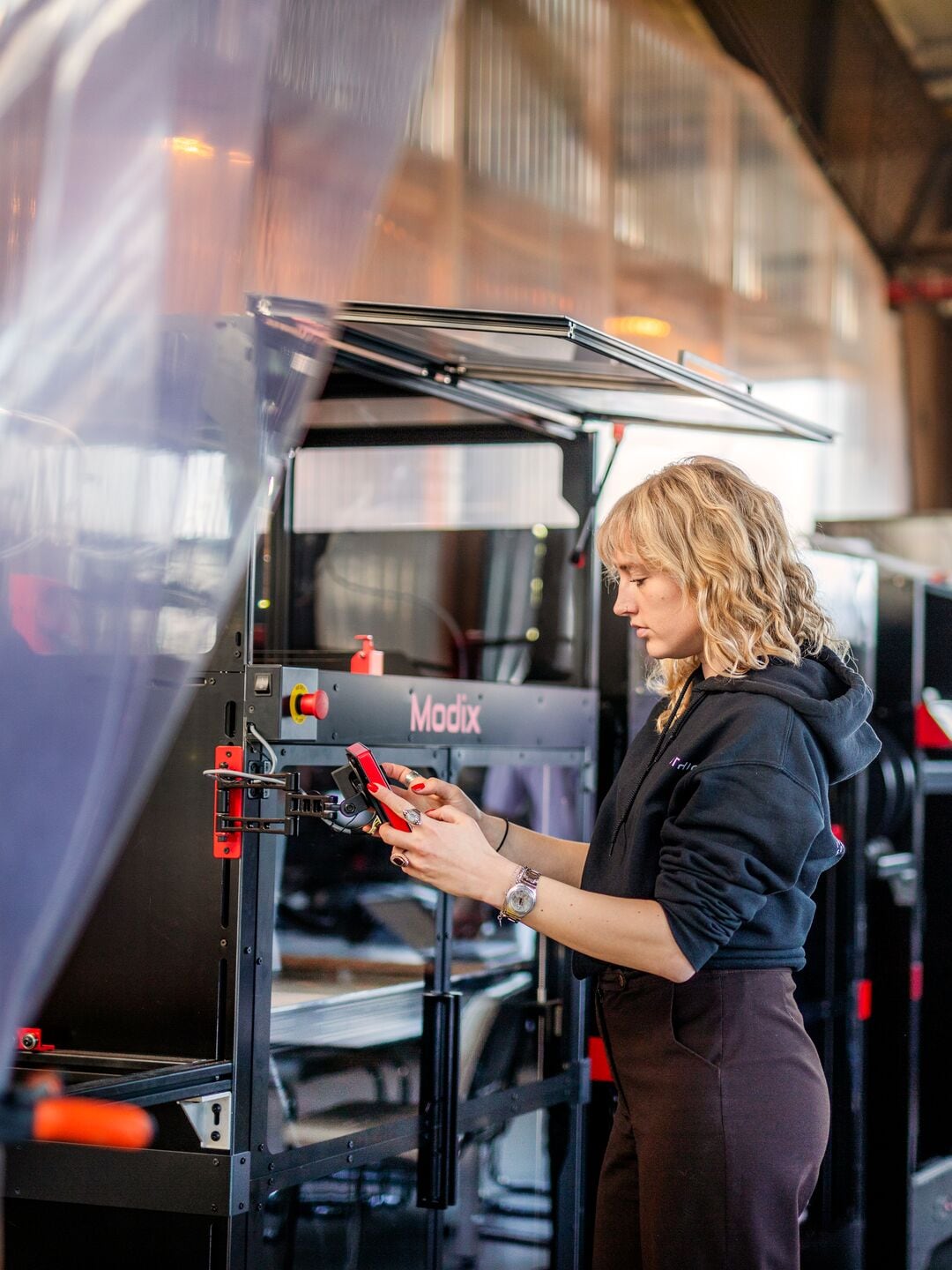 een vrouw werkt met een 3d printer, op de achtergrond hebben twee mannen overleg