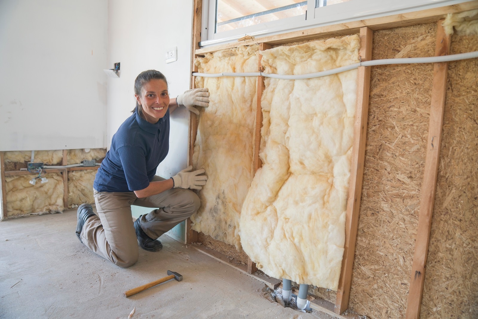 Portrait of a  female worker installing a fiberglass insulation on a wall during wood frame house construction