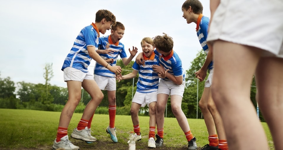 Een groep kinderen juichen op een voetbalveld 